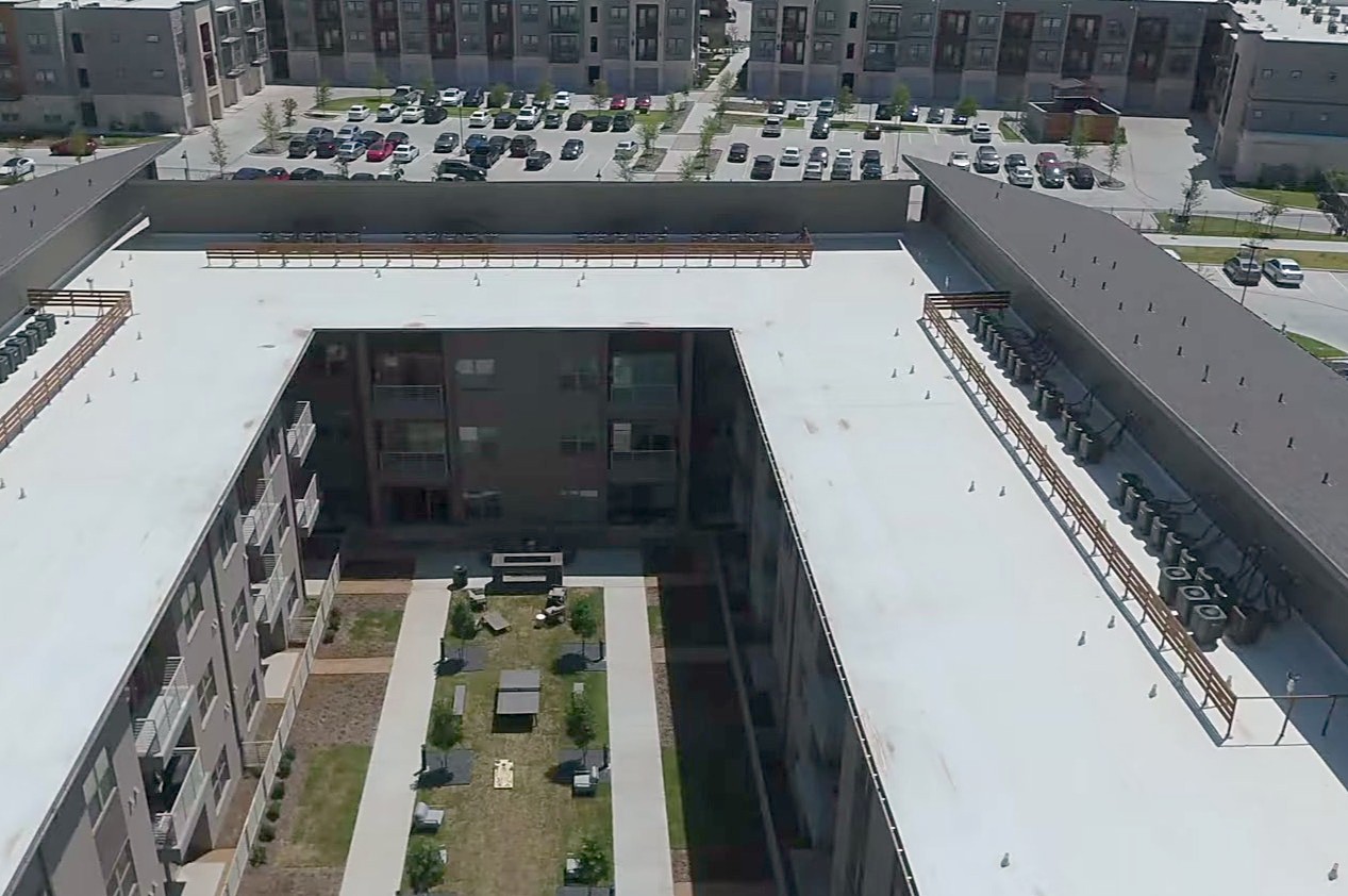 White low-slope roofs wrapping an apartment courtyard, seen from the air