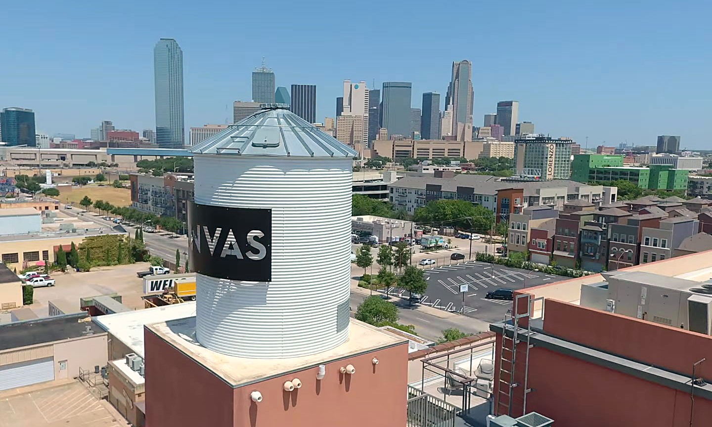 The Canvas Hotel water tower above its brick roof with the Dallas skyline behind