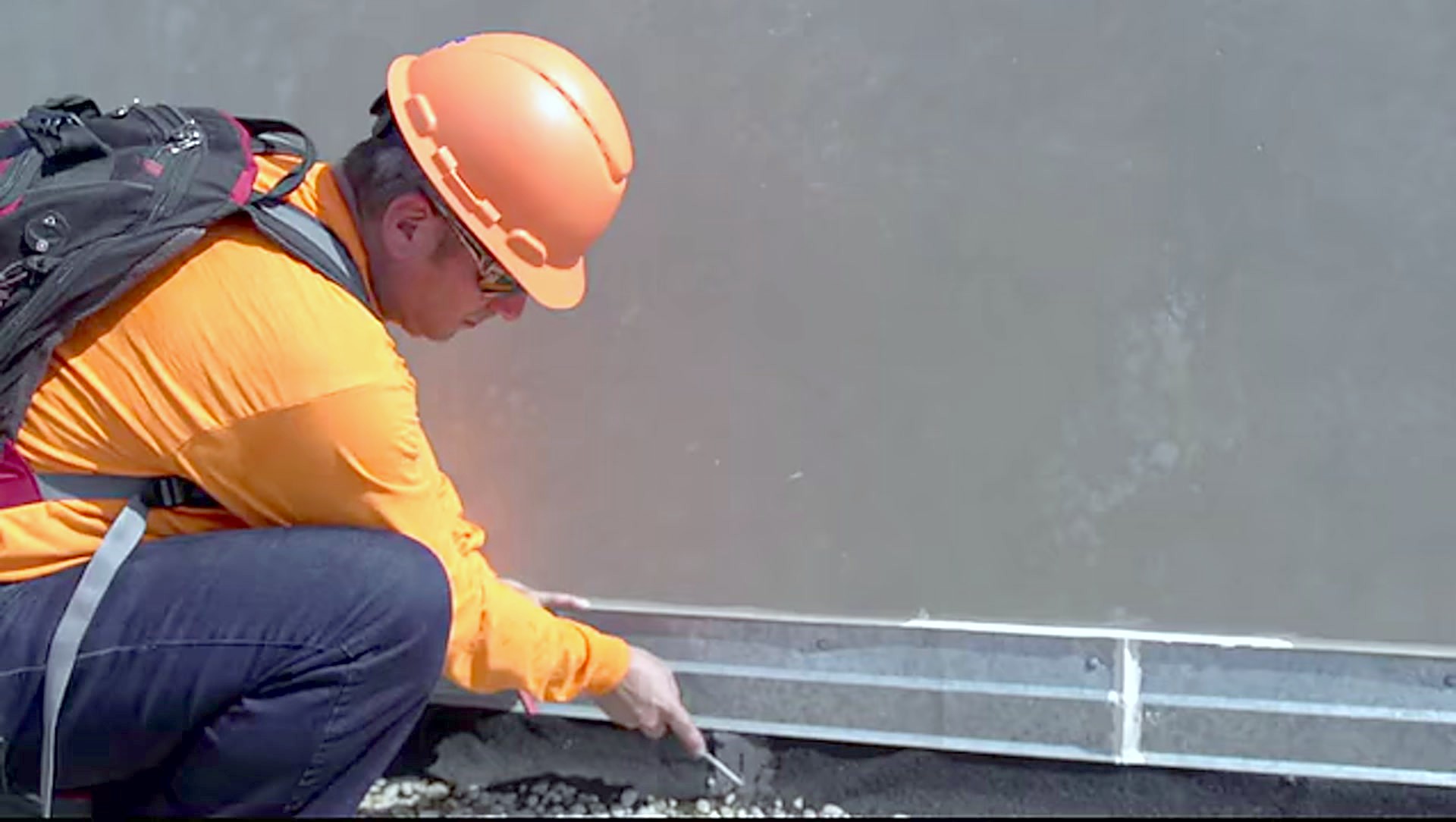 A crew member in a hard hat working along the edge metal of a roof