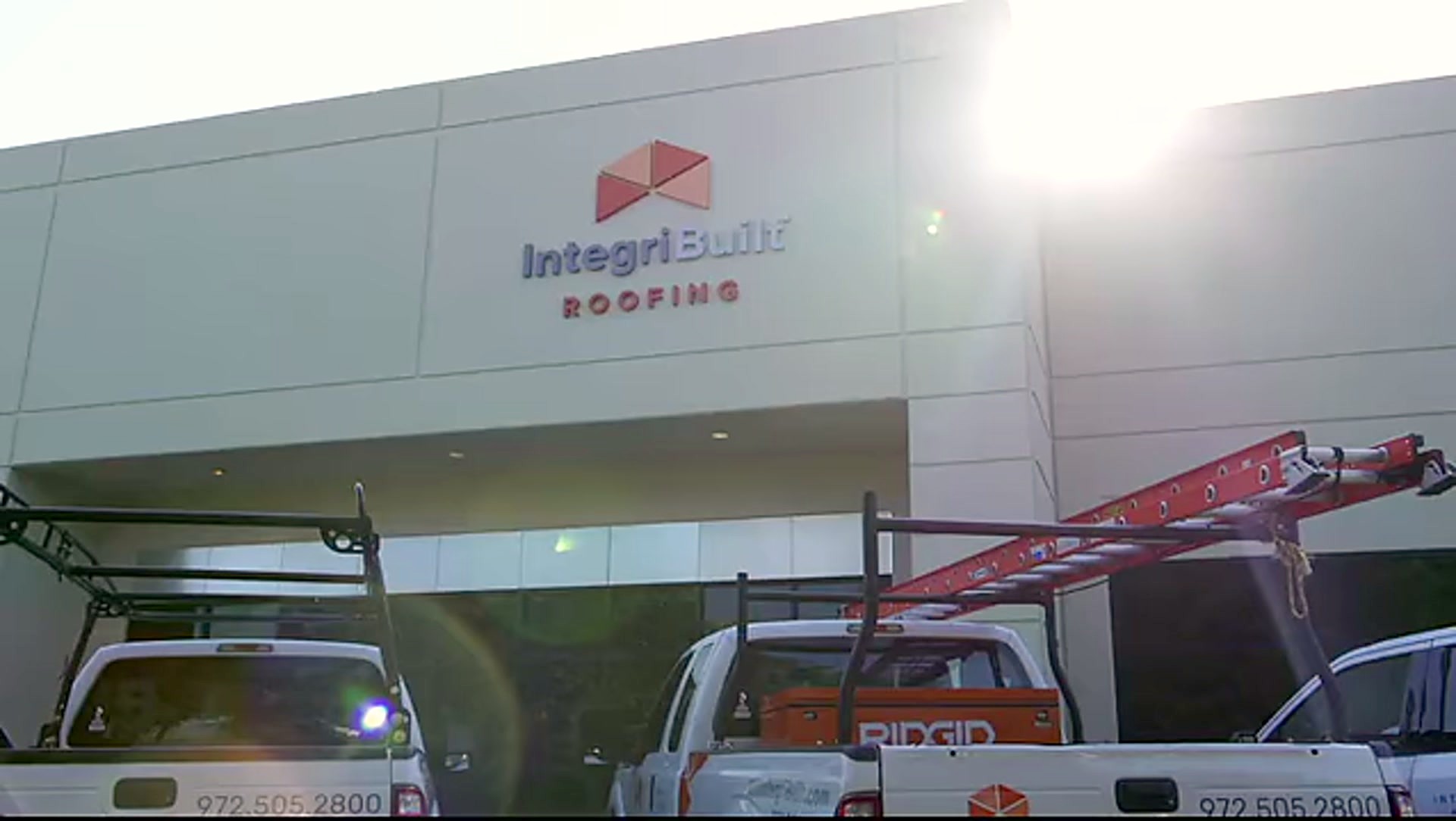 The IntegriBuilt Roofing sign above the company yard with work trucks underneath