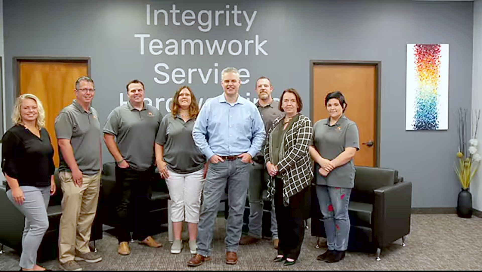 The IntegriBuilt team at the office, in front of the Integrity, Teamwork, Service wall