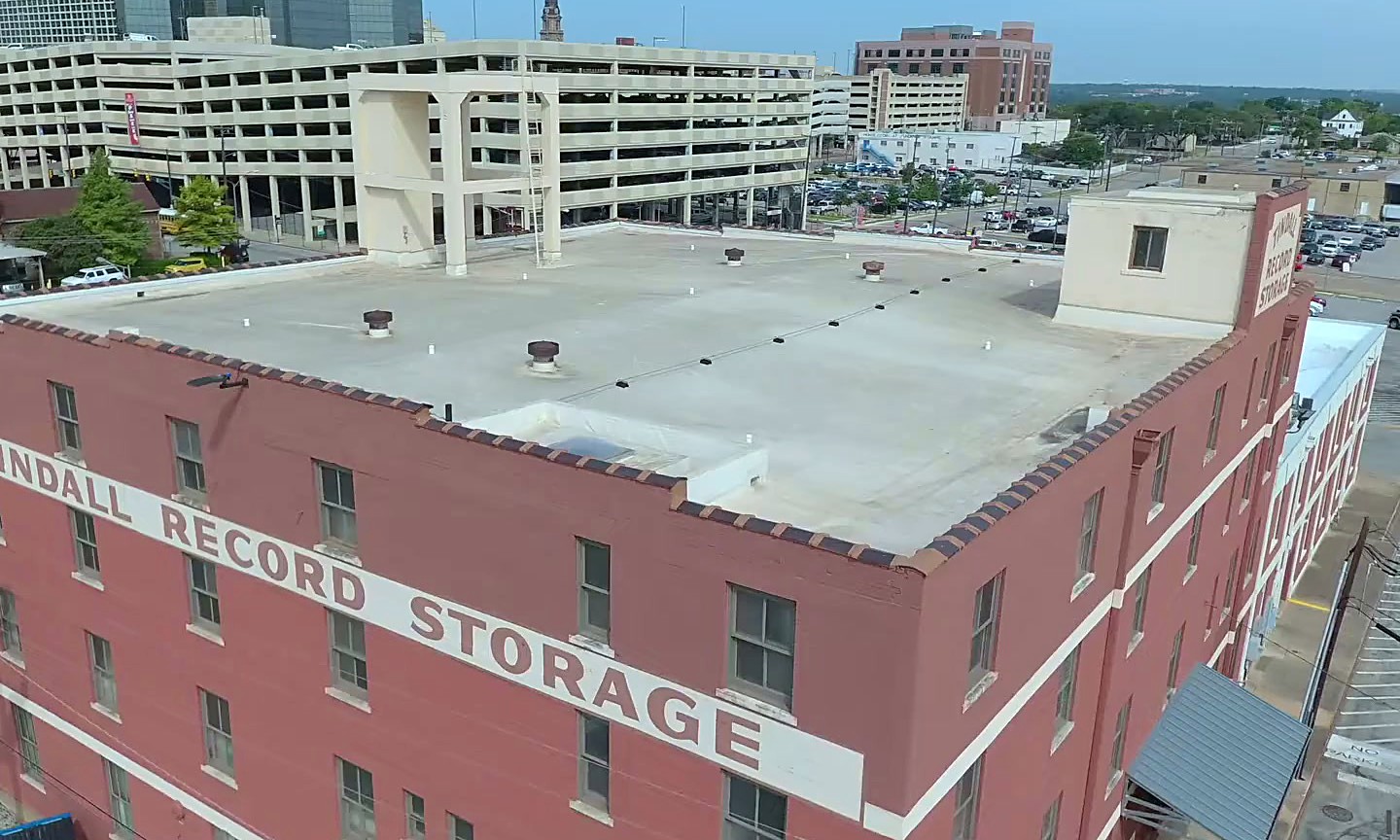 A drone view of the brick Tindall Record Storage building in Fort Worth with downtown behind it