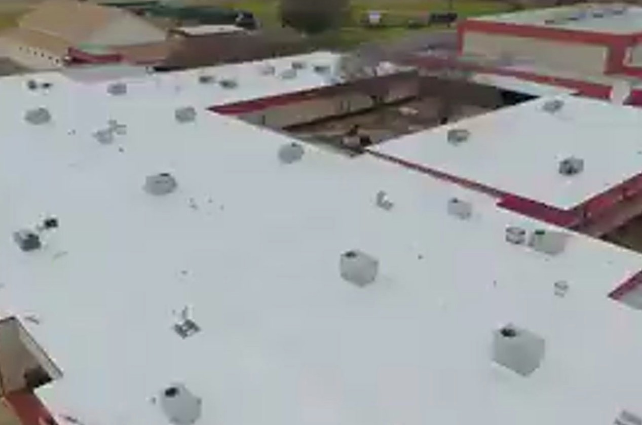 A wide white TPO roof over a school building, photographed from above